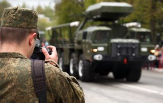 Army journalist photographer. Soldier hold professional camera and takes picture military vehicle