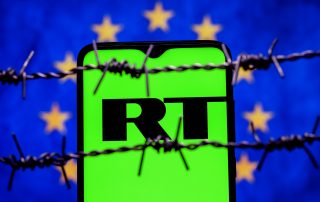 Smartphone with RT (Russia Today) logo on background of flag of European Union behind barbed wire. Russia Today network banning in EU