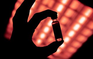 vaccine vial held against red light, showing its black silhouette