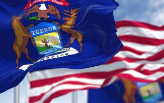 The Michigan state flag waving along with the national flag of the United States of America. In the background there is a clear sky. Michigan is a state in the upper Midwestern of United States