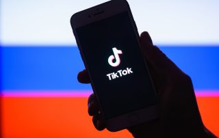 Tik Tok application on a smartphone against the background of the Russian flag.